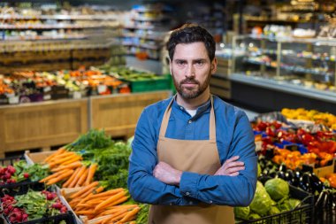 Marketteki kendine güvenen erkek çalışanın portresi taze ürünler sergiliyor. Pazar ortamında havuç, turp ve biberli önlük giyen işçiler sağlıklı yaşam tarzı besin konsepti sergiliyorlar.