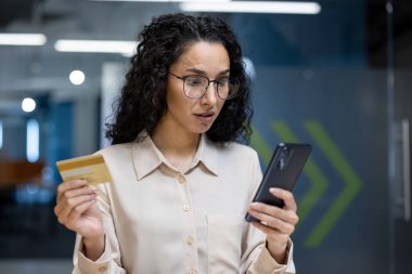 Kadın elinde kredi kartı tutarken endişeli görünüyor. Çevrimiçi işlemleri analiz ediyor, mali güvenlik, dijital ödeme riskleri ve ofisteki çevrimiçi bankacılık konularıyla ilgileniyor..