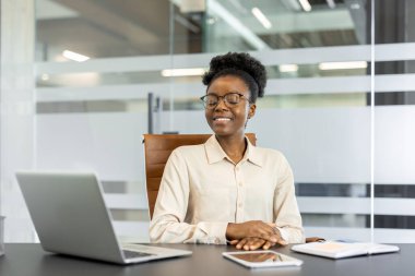 İş kadını laptopuyla masada oturuyor, gözleri kapalı, meditasyonun tadını çıkarıyor. Ofis ortamı, profesyonel kıyafetler. Çalışma alanındaki sükuneti, odaklanmayı, farkındalığı yakalar.