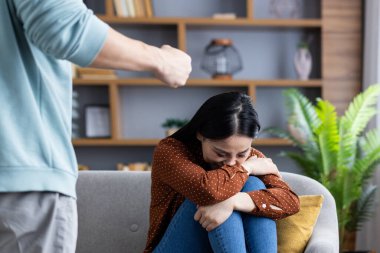 Üzgün kadın kanepeye oturmuş dizlerini tutuyor, başını eğiyor. Yakınlarda yumruğunu sıkmış biri var. Gerginlik ya da çatışmaya işaret ediyor. Sahne korku, üzüntü ve kırılganlık hissi verir..