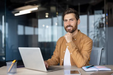 Modern ofiste dizüstü bilgisayarla ilgilenen genç bir profesyonel. Pozitif ifade odaklanmayı ve üretkenliği gösterir. Akıllı telefon, kırtasiye, çalışma alanını geliştirme, verimli sağlama