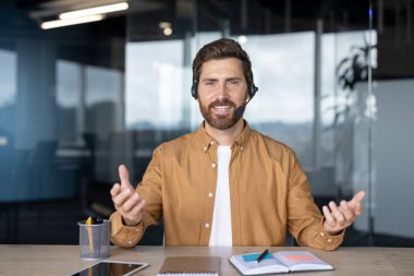Kulaklıklı gülümseyen profesyonel bir adam modern ofiste çevrimiçi bir toplantıya katılıyor. Masadaki tablet ve defter aktif katılım olduğunu gösteriyor. Özgüven, teknoloji, uzak çalışma vurgulandı.