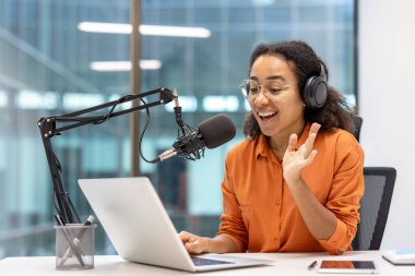 Podcast 'te mikrofon, dizüstü bilgisayar ve kulaklık takan bir kadın. Dijital içerik oluşturma, çevrimiçi yayın. Teknoloji, iletişim, yaratıcılık kavramı.