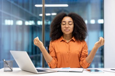 Rahat bir kadın, ofis masasında dizüstü bilgisayarın önünde meditasyon yapıyor. Farkındalık ve iş arasında iç huzuru bulmak. Sakinlik, rahatlama ve zihinsel sağlığın altını çiziyorum..