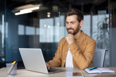 Olgun bir iş adamı dizüstü bilgisayarda çalışırken kendine güvenir ve odaklanır. Modern çalışma alanındaki ofis çalışanı işine olan bağlılığını ve düşünceli ifadesini gösteriyor..