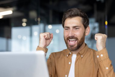 Olgun iş adamı heyecanlı yumruklar ve neşeli ifadeler sergiliyor. Kutlama, profesyonel ortamdaki zafer, başarı, başarı, motivasyon ve olumlu zihniyeti vurguluyor.