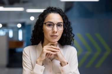 Kendine güvenen kıvırcık saçlı, ofis ortamında gözlük takan, profesyonellik ve liderlik saçan bir iş kadını. Profesyonel giysilerdeki dengeli ifadesi odaklanmayı ve kararlılığı ifade ediyor..