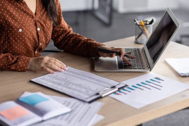Genç İspanyol iş kadını modern ofis masasında dizüstü bilgisayar kullanıyor. Çizelgeler analiz ediliyor, odak gösteren belgeler, profesyonel çevrede ayrıntılı odaklı yaklaşım