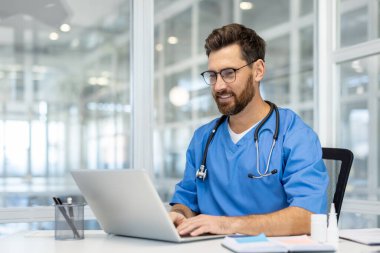 Modern ofis ortamında steteskoplu dizüstü bilgisayar kullanarak ameliyat önlükleriyle gülümseyen bir sağlık uzmanı. Tıp alanında üretkenlik, profesyonellik, sağlık ve teknoloji entegrasyonunu temsil eder.