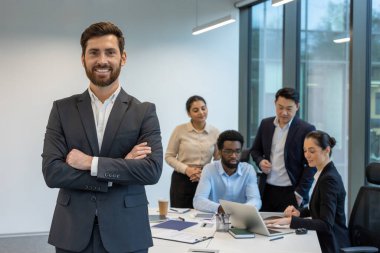 Ofis toplantısında çeşitli takımların önünde duran kendinden emin iş adamı. Grupta dizüstü bilgisayar ve akıllı telefonlardan bahseden profesyoneller de yer alıyor. Parlak, modern çalışma alanı.
