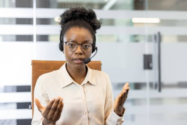 Müşteri hizmetleri temsilcisi ofiste kulaklık takıyor, sanal toplantı sırasında konuşuyor ve açıklıyor. Uzman, uzaktan yardım ve kalite iletişimi sunarak kendinden emin görünüyor.