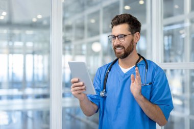 Doktor, tablet, vitrin teknolojisi ve sağlık hizmeti kullanarak görüntülü konuşma yapıyor. Mavi önlük ve steteskop giyen tıp uzmanı hastane ortamında sıcaklık ve güven yayıyor..