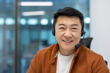 Ofiste gülümseyen kulaklıklı Asyalı bir iş adamı. Çevrimiçi toplantı ya da müşteri hizmetlerine girmek, iletişim, profesyonellik, olumlu tavır, teknoloji.