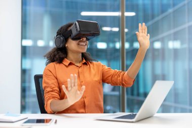 Sanal ortama dalmış VR kulaklık kullanan bir kadın. Profesyonel ortam, teknolojilerin ofis çalışmalarında yenilik, yaratıcılık ve verimlilikteki rolünü vurguluyor.