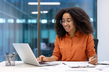 Modern çalışma ortamında kendine güvenen bir ofis çalışanı dizüstü bilgisayar kullanır ve not alır. Mesleki çevrede üretkenlik ve neşeyi somutlaştırıyor, kurumsal yaşam tarzı ve dijital iletişim sergiliyor.