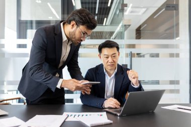 İki profesyonel bilgisayar ve akıllı telefon kullanarak modern ofiste işbirliği yaparak takım çalışması, teknoloji ve verimliliği vurguluyor. Nişanlı yöneticiler fikirleri tartışıyor, iş stratejilerini sergiliyorlar