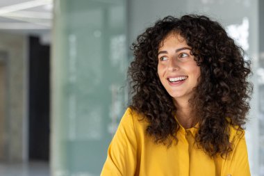 Modern, profesyonel ortamlarda gülümseyen genç bir kadın. İfadesi güven ve pozitiflik taşıyor, arkadaşlığı ve sıcaklığı arttırıyor..
