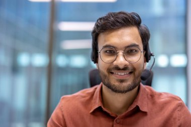 Gözlüklü, gülümseyen çağrı merkezi çalışanı. Modern ofis ortamında kendinden emin ve arkadaş canlısı olan kişi, olağanüstü müşteri hizmetleri ve iletişim uzmanlığı sunar..