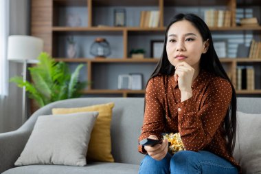 Asyalı kadın elinde uzaktan kumandayla evde televizyon seyrediyor ve patlamış mısırın tadını çıkarıyor. Rahat bir koltukta oturmak, düşünceli ve rahat bir ev ortamında. Rahat ve rahat..