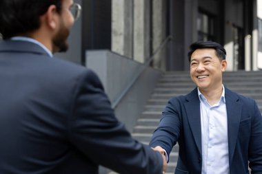 Resmi giyinmiş, el sıkışan iki iş adamı başarılı bir ortaklığı simgeliyor. Açık hava ayarı ve parlak gülümsemeler güven, bağlantı ve işbirliği sağlar..