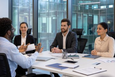 Üretken bir ofis toplantısında, takım çalışması ve işbirliğine odaklanan çeşitli bir ekip. Gülümseyen profesyoneller fikir alışverişinde bulunur, olumlu bir iş ortamı oluştururlar.