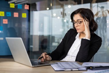 İş kadını ofis masasında yoğunlaşıyor, belgeleri analiz ediyor, dizüstü bilgisayar kullanıyor. Profesyonel, odaklanmış ve modern ofiste kararlı. İş, şirket ve profesyonel kavramlar için uygundur..