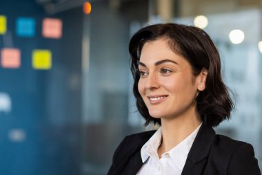 İş kadını ofiste kendine güvenerek gülümsüyor, profesyonellik ve pozitiflik yayıyor. Çalışan iş ortamında başarı, hırs ve iyimserliği somutlaştırıyor..