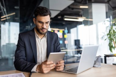 Bir iş adamı, modern ofis ortamında tabletine odaklanır, iş yerindeki teknoloji ve verimliliği vurgular.