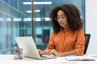 Ofis masasında dizüstü bilgisayarla çalışan genç profesyonel bir kadın. Başarılı bir iş ortamının niteliklerini somutlaştırarak odaklanma ve adanmışlık gösteriyor..