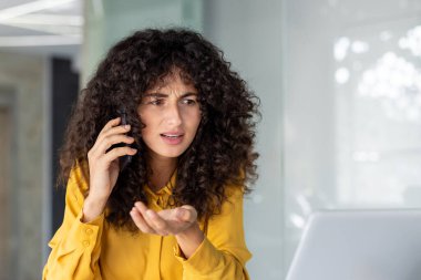 Kafası karışmış bir kadın telefonuyla konuşuyor. Bilgisayarlı modern bir ofis ortamında, muhtemelen şaşırtıcı bir durumla uğraşıyor..