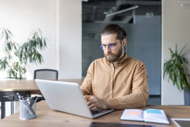 Modern ofisteki bir masada dizüstü bilgisayar kullanarak profesyonelce odaklanmış. Profesyonel bir çalışma alanında üretkenlik, iş ve teknoloji kullanımı kavramı.