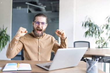 Ofis ortamında neşeli bir adam başarısını gözle görülür bir hevesle kutluyor, dizüstü bilgisayarla çalışıyor. İmaj motivasyonu, iş başarısını ve işte anlık zaferi yakalıyor..