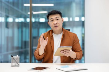 Asyalı adam konseptleri özgüvenle açıklıyor. İş toplantısı, işbirliği ve takım çalışmasını vurguluyor.