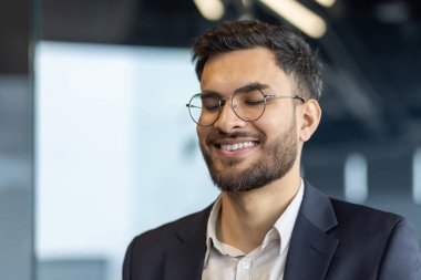 Olgun iş adamı gözleri kapalı gülümsüyor, ilham ve memnuniyet saçıyor. Parlak bir gülümseme ile resmi giysiler içinde profesyonel pozitifliği somutlaştırıyor..