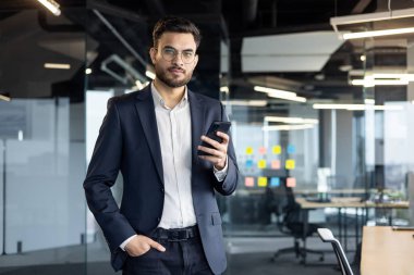 Ofiste telefon kullanan olgun bir profesyonel. Çevre, modern profesyonel iş kültürünü sembolize ederek verimlilik ve odaklanmayı öneriyor. Birey kendinden emin ve bağlı görünüyor.