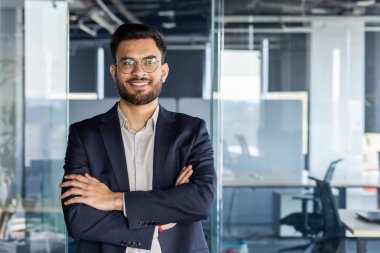 Kendinden emin, olgun bir iş adamı kolları bağlı bir şekilde ofis ortamında poz verdi. İmaj profesyonellik, güven ve hırs yayarak, onu iş dünyası veya liderlikle ilgili bağlamlar için ideal hale getiriyor..