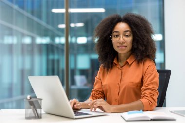 Ofiste dizüstü bilgisayarıyla çalışan profesyonel bir genç kadın, özgüven ve odaklanma yayarak, bunu iş ve profesyonellikle ilgili kavramlar için ideal bir görüntü haline getiriyor.