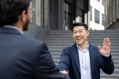 İki iş adamı dostça tokalaşıyor ve gülümsüyor açık şehir ortamında. Sahne profesyonel nezaketin, ağ kurmanın ve başarılı işbirliğinin özünü yakalıyor.