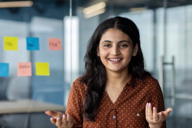 Modern bir iş ortamında dostça ve açık bir tavırla güven ve ulaşılabilirliği ifade eden profesyonel birey, etkili iletişim ve insanlar arası becerileri vurguluyor.