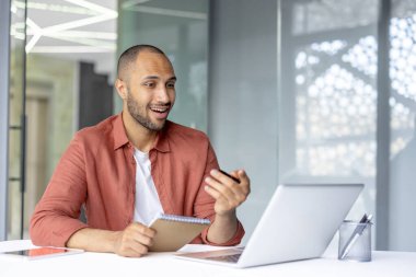 İş yerinde eğitim videosu izleyen adam online seminer webinar, not defteri ile iş adamı ofiste dizüstü bilgisayarla otururken veri yazıyor..