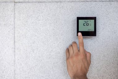 Bir insan, dokulu bir duvara monte edilmiş dijital termostatı ayarlar ve derece olarak Celsius 'u gösterir..