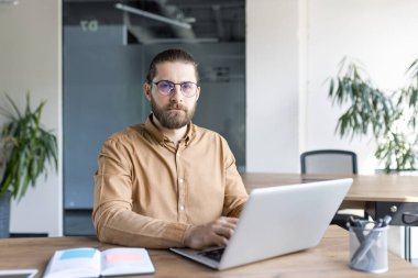 Ofis malzemeleri ve bitkilerle çevrili bir dizüstü bilgisayarda çalışan odaklanmış bir profesyonel. Sunumlar ve reklamlar için iş dünyası, teknoloji ve ofis teması için mükemmel bir imaj.