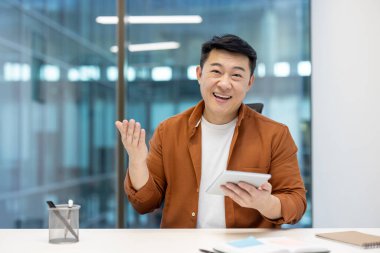 Asyalı bir adam ve yetişkin bir işadamı kameraya bakıyor ve akıllı telefon kullanarak iletişim kuruyor. Profesyonel ofis ortamında neşeli ve çekici bir tavır sergiliyor..