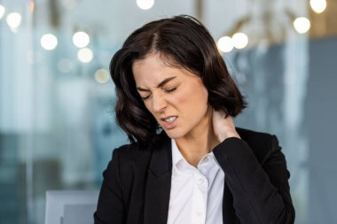 Ofisteki genç iş kadını boynu ağrıyan uzun masa başı işlerinden rahatsız olduğunu ifade ediyor. Resim, ergonomik çözümlere duyulan ihtiyacı vurgulayarak, profesyonel ortamdaki stres ve gerginliği yakalar.