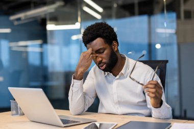 Yorgun ve çok çalışan bir adam masada oturuyor, başı dönen bir iş adamı dizüstü bilgisayarla oturuyor, göz ağrısı çekiyor, akşama kadar geç saatlere kadar çalışıyor..