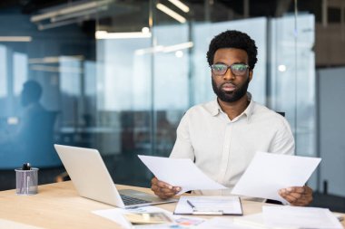 Ciddi odaklı muhasebeci portresi evrak işleri yapıyor, elinde mali raporlar tutan adam kameraya bakıyor, işadamı evrak işleriyle uğraşıyor, vergi formlarını dolduruyor ve kontrol ediyor, sözleşmeler yapıyor..