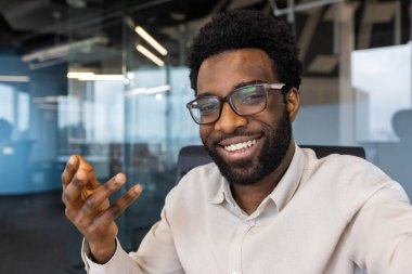 İş adamı gülümsüyor ve akıllı telefon kamerasına bakıyor. Telefondaki uygulamayı video görüşmesi için kullanıyor. İş yerindeki şirket çalışanı..