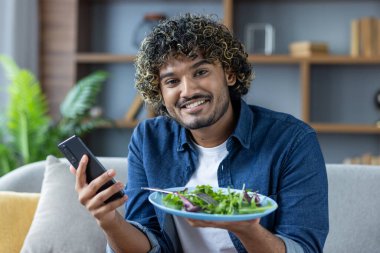 Evdeki kanepede oturup kameraya bakan bir adamın portresi. Elinde bir tabak salata, internette sağlıklı beslenme ve beslenme üzerine bir ders izliyor..