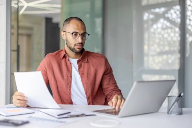 Ofis içinde evrak işleriyle uğraşan ciddi odaklı bir işadamı, günlük gömlekli bir adam belge sözleşmeleri ve raporlarla çalışıyor, başarılı bir yatırımcı..