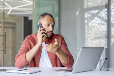 Ofisteki bir masada elinde not defteriyle oturan ciddi odaklanmış bir adam. Günlük gömlekli bir ofis çalışanı..